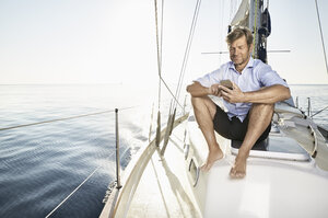 Smiling mature man sitting on his sailing boat using cell phone - PDF01159