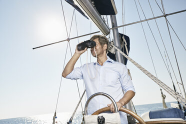 Älterer Mann mit Fernglas am Ruder seines Segelboots - PDF01178