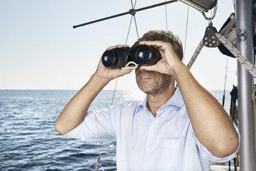 Mature man using binoculars on his sailing boat - PDF01179