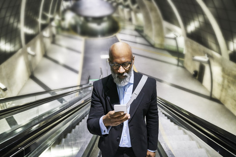 Geschäftsmann mit Smartphone liest Nachrichten auf der Rolltreppe, lizenzfreies Stockfoto