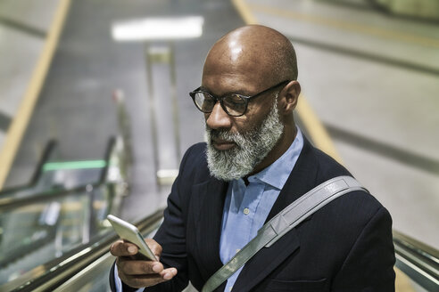 Businessman with smartphone reading messages on escalator - FMKF03786