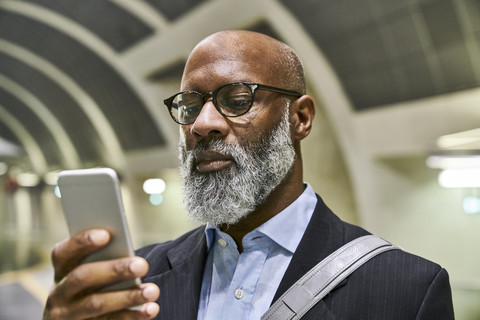 Geschäftsmann mit Smartphone liest Nachrichten auf der Rolltreppe, lizenzfreies Stockfoto