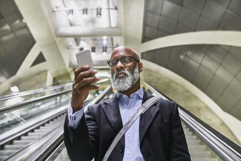 Geschäftsmann mit Smartphone liest Nachrichten auf der Rolltreppe - FMKF03788