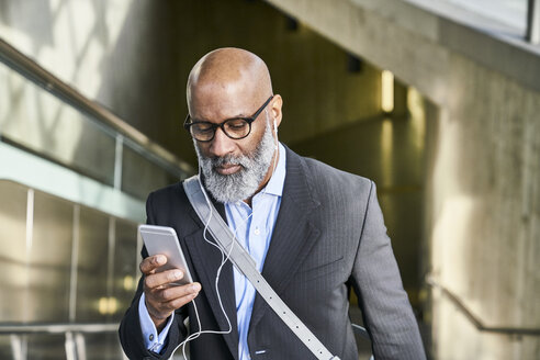 Geschäftsmann mit Smartphone liest Nachrichten auf der Rolltreppe - FMKF03789