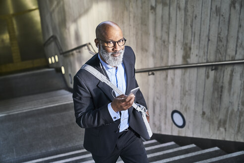 Businessman with crossbody bag using smartphone - FMKF03792