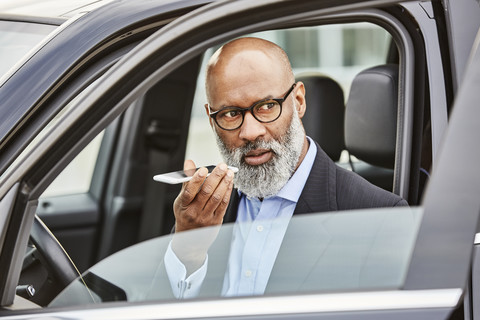 Geschäftsmann sitzt im Auto und benutzt sein Smartphone, lizenzfreies Stockfoto