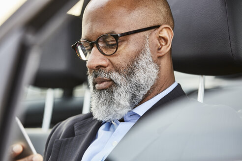 Businessman sitting in car using smartphone - FMKF03802