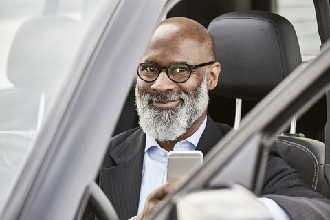 Businessman sitting in car using smartphone stock photo