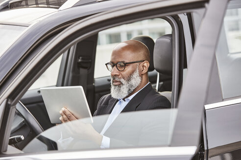 Geschäftsmann im Auto sitzend mit digitalem Tablet - FMKF03804