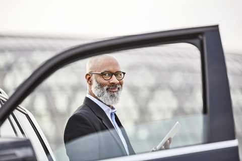 Geschäftsmann mit digitalem Tablet neben einem Auto stehend, lizenzfreies Stockfoto