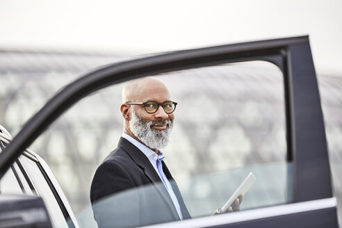 Businessman with digital tablet standing by car - FMKF03805