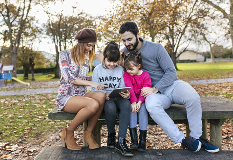 Familie sitzt auf einer Bank im herbstlichen Park und schaut auf eine Tafel - MGOF03183