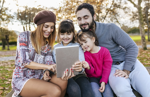 Familie sitzt auf einer Bank im herbstlichen Park und macht ein Selfie mit einem Tablet, lizenzfreies Stockfoto