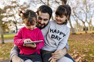 Father with his little daughters looking at tablet in autumnal park - MGOF03195