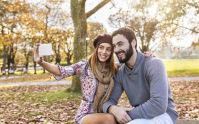 Glückliches Paar macht Selfie mit Smartphone im herbstlichen Park - MGOF03199