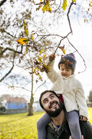 Kleines Mädchen auf den Schultern ihres Vaters im herbstlichen Park, lizenzfreies Stockfoto