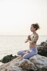 Woman sitting in lotus seat, meditating on the beach - MOMF00067