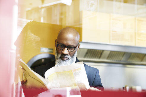 Älterer Geschäftsmann sitzt in einer Snackbar und liest Zeitung - FMKF03813