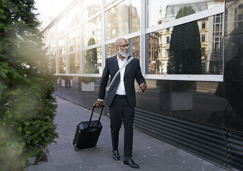 Mature businessman walking in street, pulling trolley bag - FMKF03825