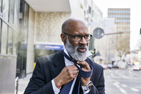 Älterer Geschäftsmann bindet Krawatte auf der Straße - FMKF03834
