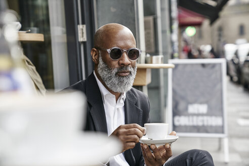 Älterer Geschäftsmann trinkt Kaffee in einem Straßencafé - FMKF03850