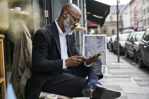 Älterer Geschäftsmann sitzt in einem Café und benutzt ein digitales Tablet - FMKF03851
