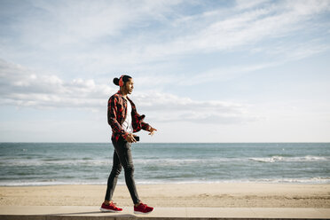 Junger Mann geht auf der Mauer vor der Strandpromenade und hört Musik mit Kopfhörern - JRFF01291