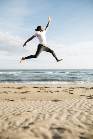 Junger Mann springt am Strand in die Luft, lizenzfreies Stockfoto