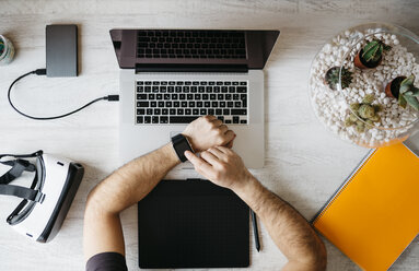 Man using smartwatch at desk, top view - JRFF01303