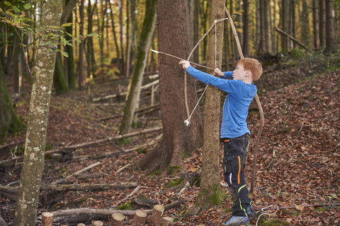 Junge zielt mit Bogen im Wald, lizenzfreies Stockfoto