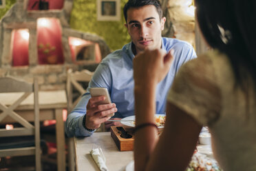 Mann mit Handy, der seiner Freundin in einem Restaurant gegenübersitzt - MOMF00108