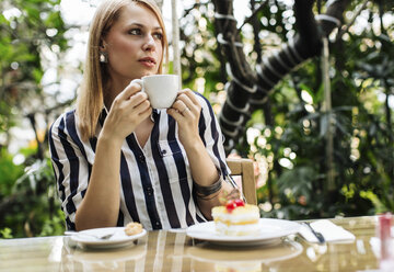 Frau sitzt in einem Straßencafé mit Kuchen und einer Tasse Kaffee - MOMF00117