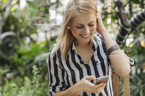 Glückliche blonde Frau schaut auf ihr Smartphone - MOMF00118