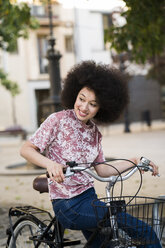 Porträt einer lächelnden jungen Frau, die auf einem Fahrrad sitzt und etwas beobachtet - KKAF00700