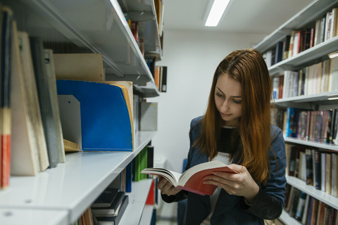 Studentin beim Lesen eines Buches in einer Bibliothek, lizenzfreies Stockfoto