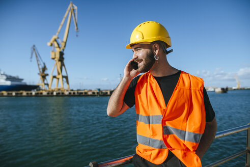 Lächelnder Hafenarbeiter, der mit seinem Handy telefoniert - KIJF01381
