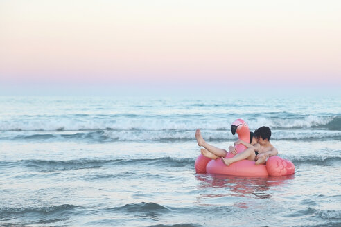 Verliebtes Paar schwimmt mit aufblasbarem rosa Flamingo auf dem Meer bei Sonnenuntergang - RTBF00819