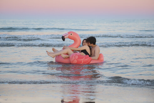 Verliebtes Paar schwimmt mit aufblasbarem rosa Flamingo auf dem Meer bei Sonnenuntergang - RTBF00820