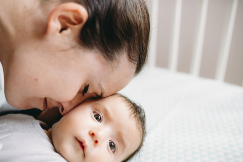 Mutter streichelt ihr Baby in der Krippe, lizenzfreies Stockfoto