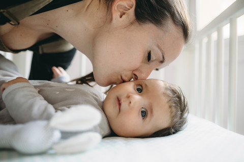 Mutter küsst ihr Baby in der Krippe, lizenzfreies Stockfoto