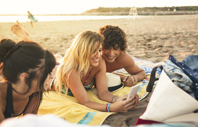 Smiling young man and woman sharing cell phone on the beach - DAPF00677