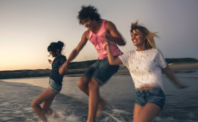 Happy friends holding hands and running into the sea at dusk - DAPF00681