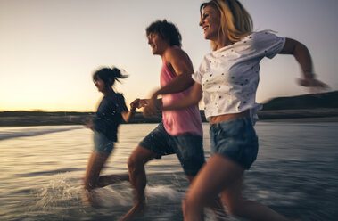 Happy friends holding hands and running into the sea at dusk - DAPF00682