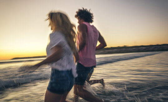 Freunde, die sich an den Händen halten und in der Abenddämmerung ins Meer laufen - DAPF00683