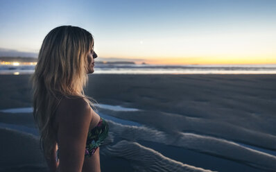 Junge Frau beobachtet den Sonnenuntergang am Strand - DAPF00691