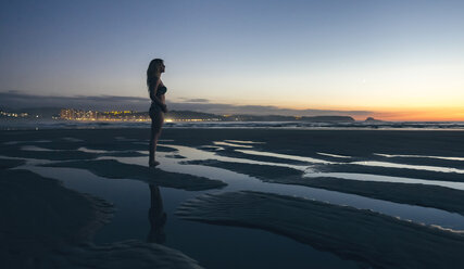 Junge Frau beobachtet den Sonnenuntergang am Strand - DAPF00692