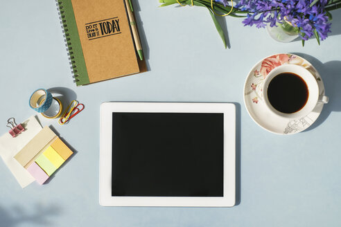 Tablet, Notebook, Büromaterial, Tasse Kaffee und Frühlingsblumen auf hellblauem Hintergrund - MOMF00131