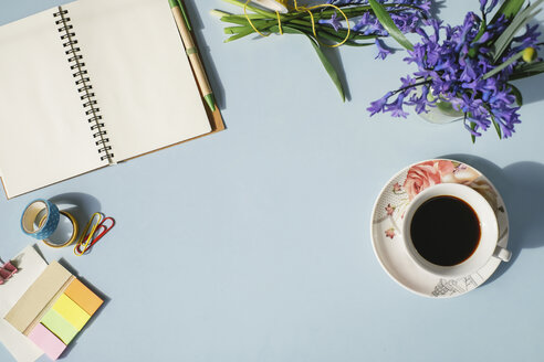 Notebook, Büromaterial, Tasse Kaffee und Frühlingsblumen auf hellblauem Hintergrund - MOMF00135