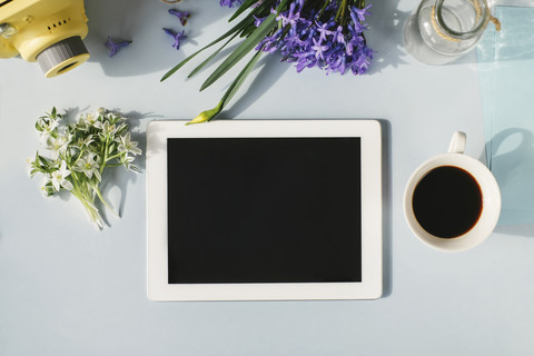 Tablet, Kamera, Tasse Kaffee und Frühlingsblumen auf hellblauem Hintergrund, lizenzfreies Stockfoto