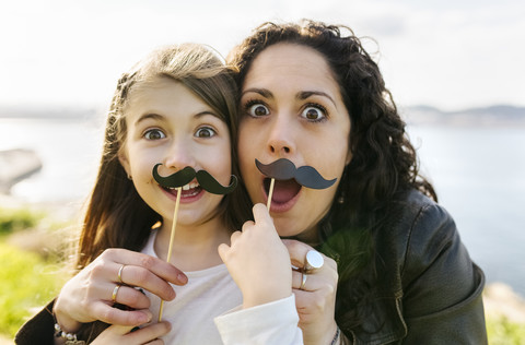 Mutter und Tochter haben Spaß mit falschen Schnurrbärten, lizenzfreies Stockfoto